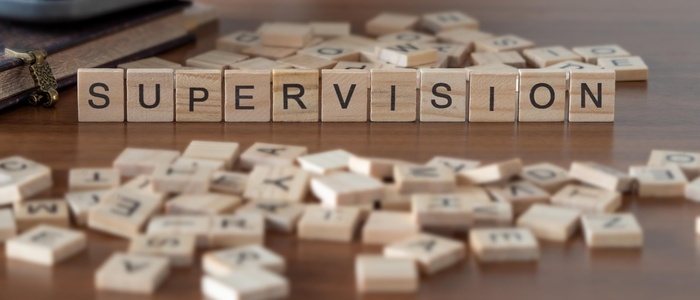 supervision word or concept represented by wooden letter tiles on a wooden table with glasses and a book